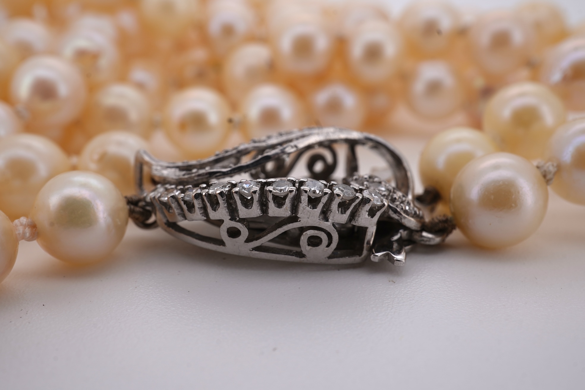 A twin strand cultured pearl necklace with a diamond cluster set white metal scroll shaped clasp, 60cm.